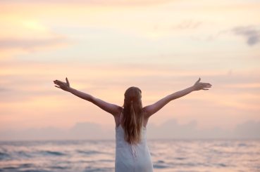 rear-view-of-woman-with-arms-raised-at-beach-during-sunset-320007